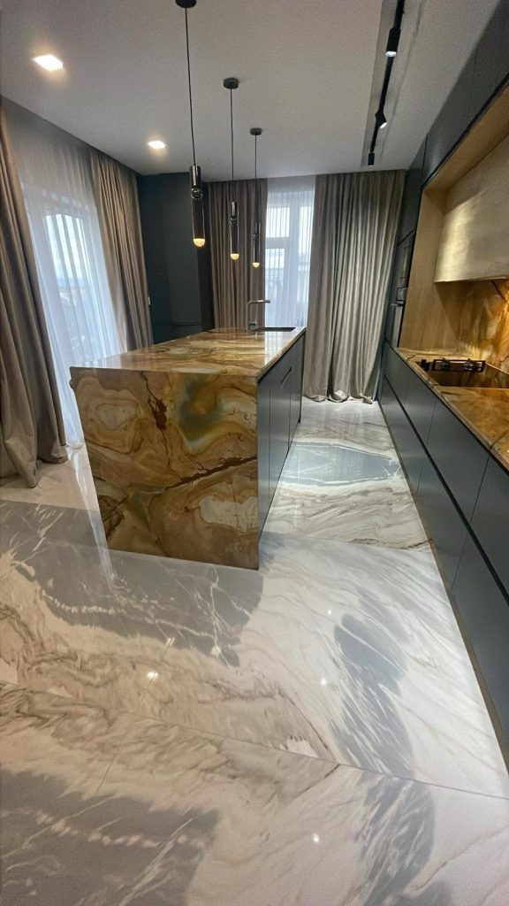 Pardoseala din marmura lucioasa montata intr-o bucatarie moderna cu insula si finisaje elegante.